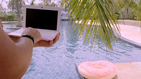 A man is typing on his laptop while sitting by the pool. Mens hands on the Stock Photos