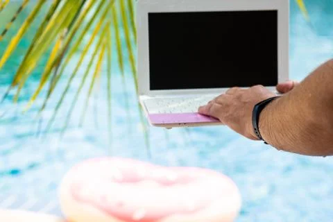 A man is typing on his laptop while sitting by the pool. Mens hands on the Stock Photos