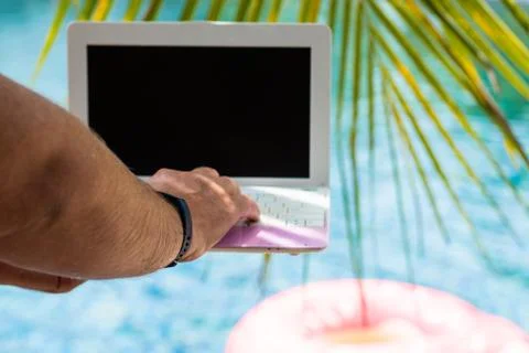A man is typing on his laptop while sitting by the pool. Mens hands on the Stock Photos