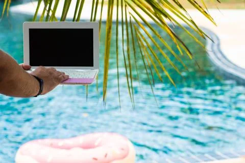 A man is typing on his laptop while sitting by the pool. Mens hands on the Stock Photos