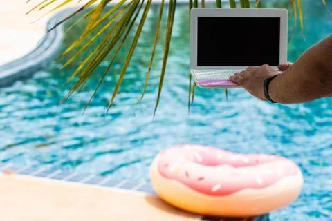 A man is typing on his laptop while sitting by the pool. Mens hands on the Stock Photos