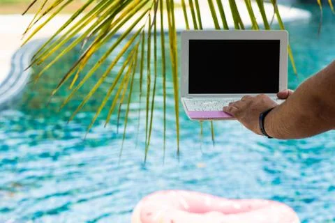 A man is typing on his laptop while sitting by the pool. Mens hands on the Stock Photos