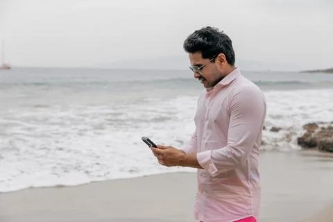 A man is typing on his phone while at the beach, it's a cloudy day Stock Photos