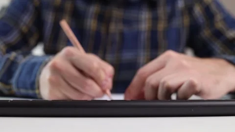 A man is typing on a keyboard and writing with a pencil while sitting at a table Stock Footage 244599183