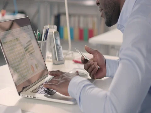 Man typing on laptop and using phone in a startup office - track left. Stock Footage 72823258