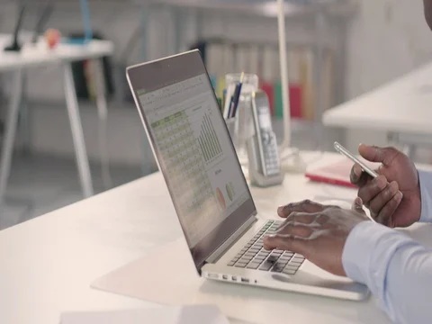 Man typing on laptop and using phone in a startup office - track right. Stock Footage 72823658