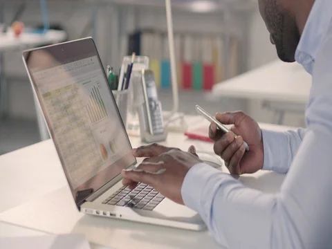 Man typing on laptop and using phone in a startup office - track left. Stock Footage 72825755