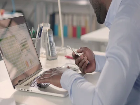 Man typing on laptop and using phone in a startup office. Stock Footage 72831549
