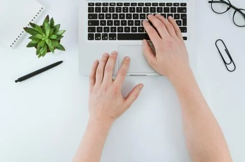Man typing on laptop computer over white office desk table with green plant. Top Stock Photos
