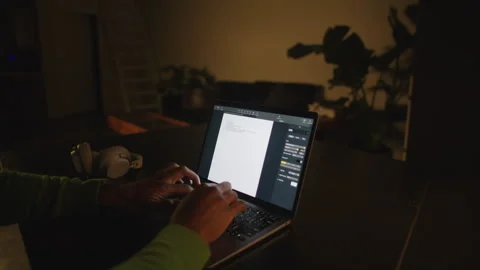 Man typing on laptop at a dark desk in a quiet room late at night Stock Footage 312583271