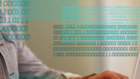 Man typing on laptop at desk, sending teal binary overlay obscuring hands face Stock Footage 333774516