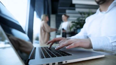 A man is typing on a laptop in front of a window Stock Photos