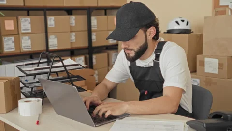 Man typing on laptop with hands amid parcels, stacked boxes, label roll and.. Stock Footage 337371789