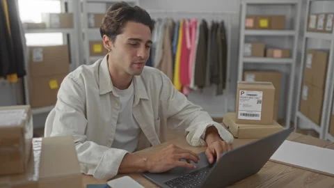 Man typing on laptop with hands on keyboard and shipping boxes stacked near.. Stock Footage 337436376