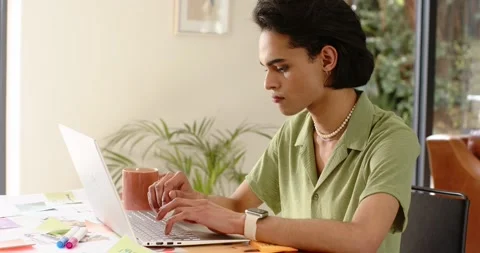 Man typing on laptop at home table glancing sticky note resuming typing and Stock Footage 345071119