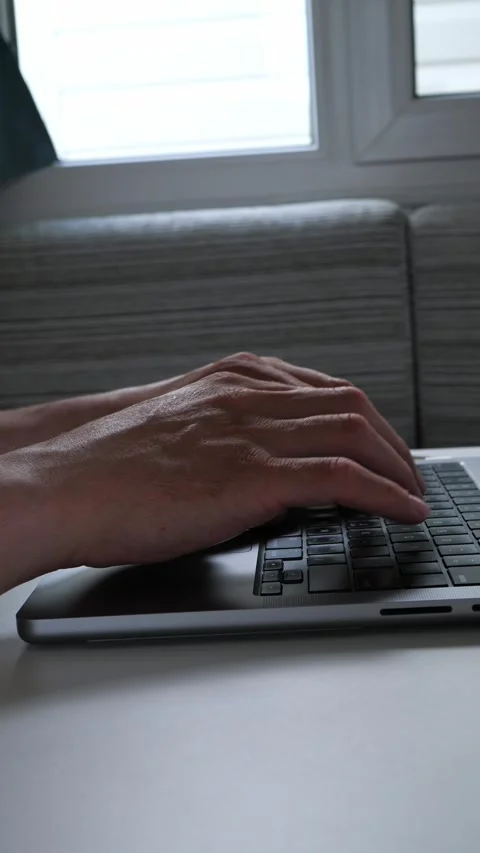 Man typing on laptop keyboard working from home by a window Stock Footage 342640708