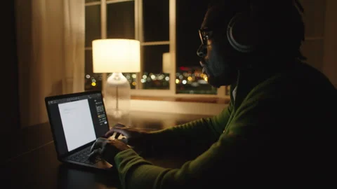 Man typing on laptop at night with lamp illuminating workspace Stock Footage 312584443