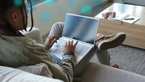 Man typing on laptop on sofa initiating wireframe graphics and blue streaks for Stock Footage 333720232