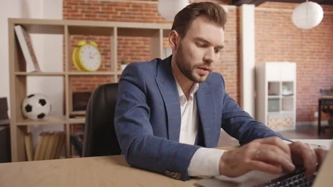A man typing on a laptop, someone throws papers with reports on the table Stockbeeldmateriaal 190994989