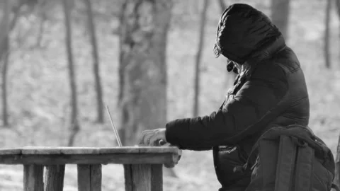 Man typing on a laptop at a table in the forest, side view, in black and whi Vídeos de archivo 174842979