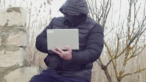 Man typing on a laptop while sitting on a collapsed wall Vídeos de archivo 174843224