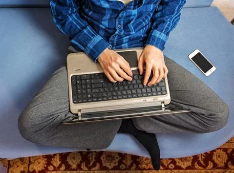 A man is typing on a laptop while sitting on the couch Foto stock