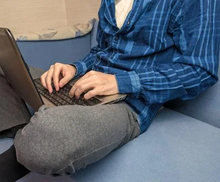 A man is typing on a laptop while sitting on the couch Stock Photos