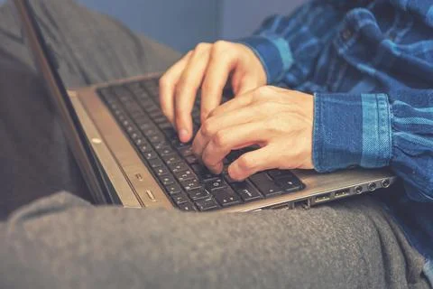 A man is typing on a laptop while sitting on the couch. Vintage tinted glass. Stock Photos