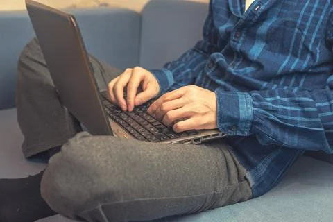A man is typing on a laptop while sitting on the couch. Vintage tinted glass. Stock Photos