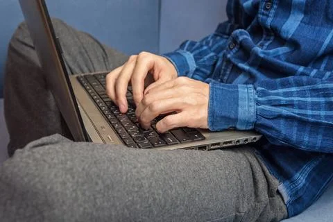 A man is typing on a laptop while sitting on the couch Stock Photos