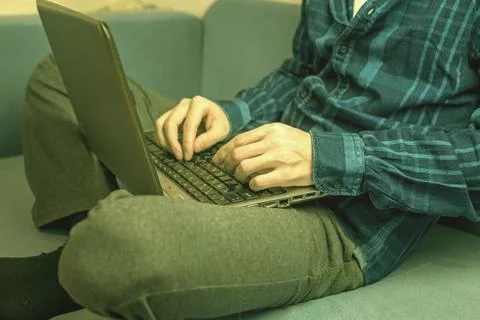 A man is typing on a laptop while sitting on the couch Stock Photos