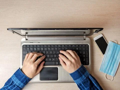 A man is typing on a laptop while sitting on the couch. The medical mask is n Stock Photos