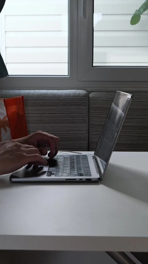 Man typing on a laptop at a white table beside a bright window Stock Footage 343566384