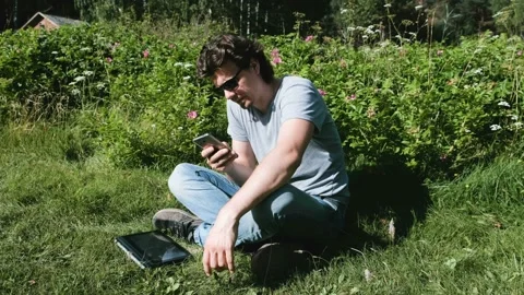 Man is typing a message on mobile phone sitting in park in sunny day. Freelance Stock-Footage 102450488