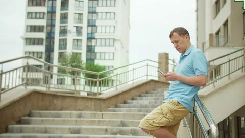 Man typing a message in a phone while standing on the stairs of a building Stock Footage 153055792