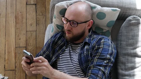 Man typing a message on the phone while lying on the couch. 库存影片 254910761