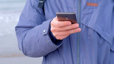 Man typing message on smartphone in coastal town at sea in winter, hands clseup. Stock Footage 117904241