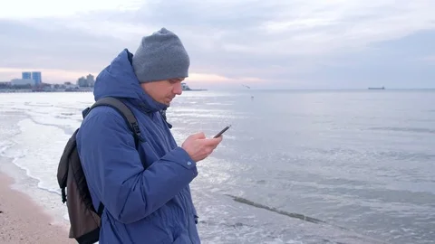 Man is typing message on smartphone in coastal town at sea in winter. Stock Footage 117907141