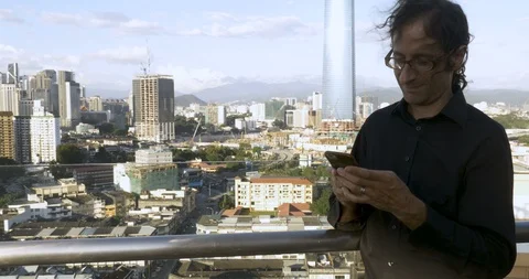 Man typing on a mobile phone overlooking a large city looks up at the camera Stock Footage 86713365