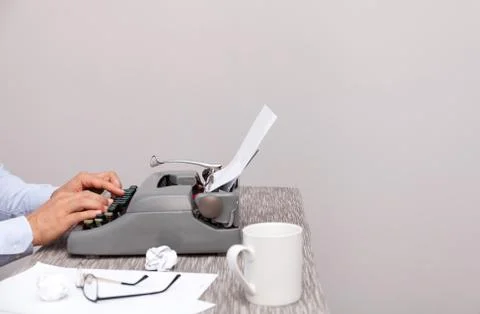 The man typing on an old-fashioned typewriter. On the table are glasses and Stock Photos