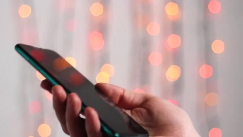 Man is typing SMS on mobile phone against the background of New Year's lights. Stock Footage 143379105