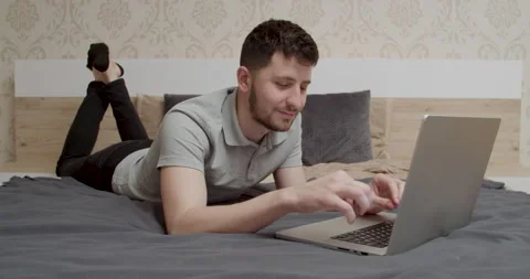 Man typing text on laptop keyboard lying on bed. Boy working with laptop in bed Stock Footage 196000478
