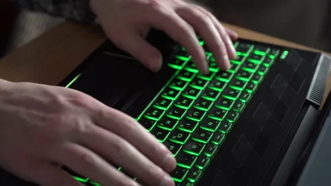 A man is typing text on a laptop keyboard with green backlight. close-up. Stock Footage 237017685