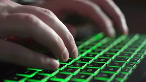 A man is typing text on a laptop keyboard with green backlight. close-up. Stock Footage 237450899