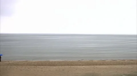 A man with an umbrella walking on the beach 스톡 동영상 11312523