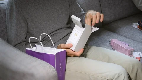 Man unboxing on the couch cosmetics containing L'Artisan Perfume Stock-Footage 86608676