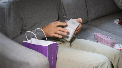 Man unboxing on the couch cosmetics containing L'Artisan Perfume Stock Footage 86608684