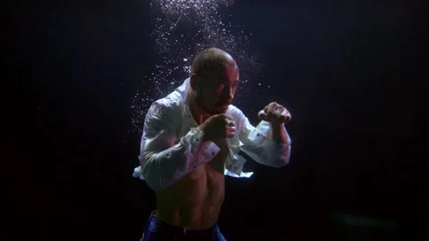 A man in an unbuttoned white shirt is boxing in dark water with bubbles. three Video stock 195080904