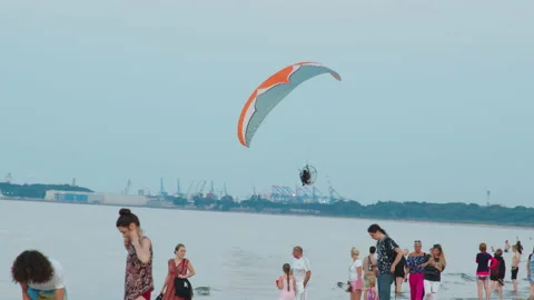 Man under the canopy of parachute flying over the beach against the clear blue Vídeos de archivo 153054871