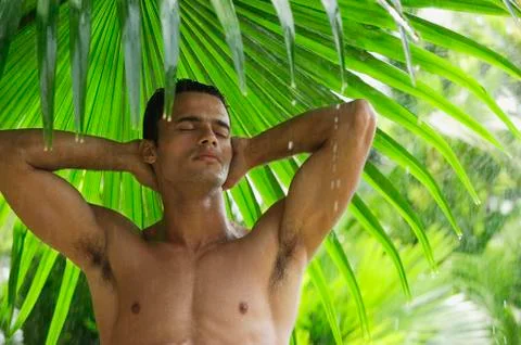 Man under giant leaf in rain shower Stock Photos